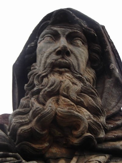 Escultura realista de anciano con barba rizada y capucha