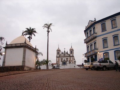 Plaza empedrada en Ouro Preto con iglesia barroca y edificio colonial bajo cielo nublado — Antônio Francisco Lisboa "Aleijadinho"