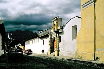 Calle colonial barroca y caminante bajo el dramático cielo nublado — Anónimo (arte colonial)